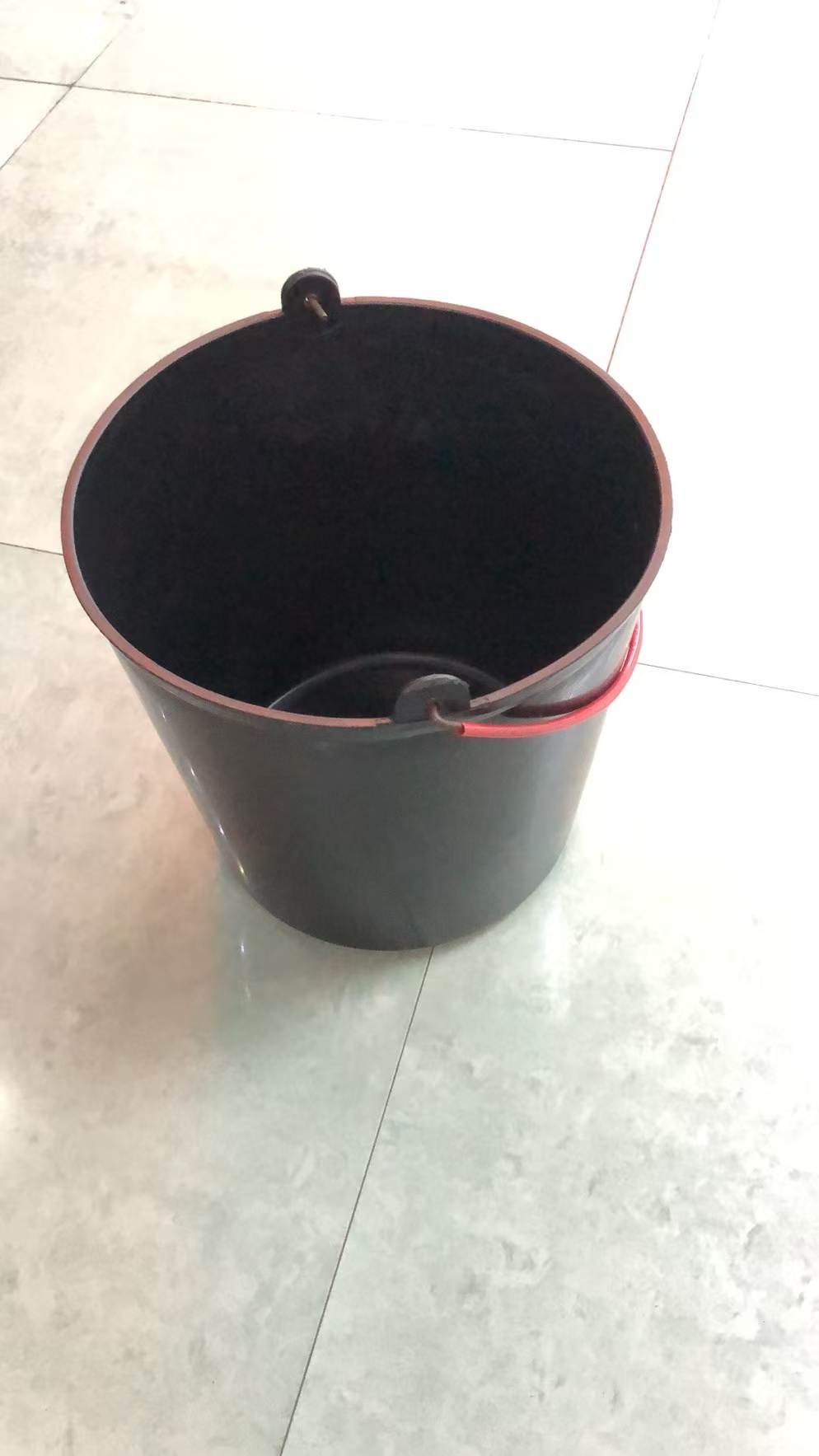 黑色塑料桶，红色提手，置于光滑瓷砖地面，